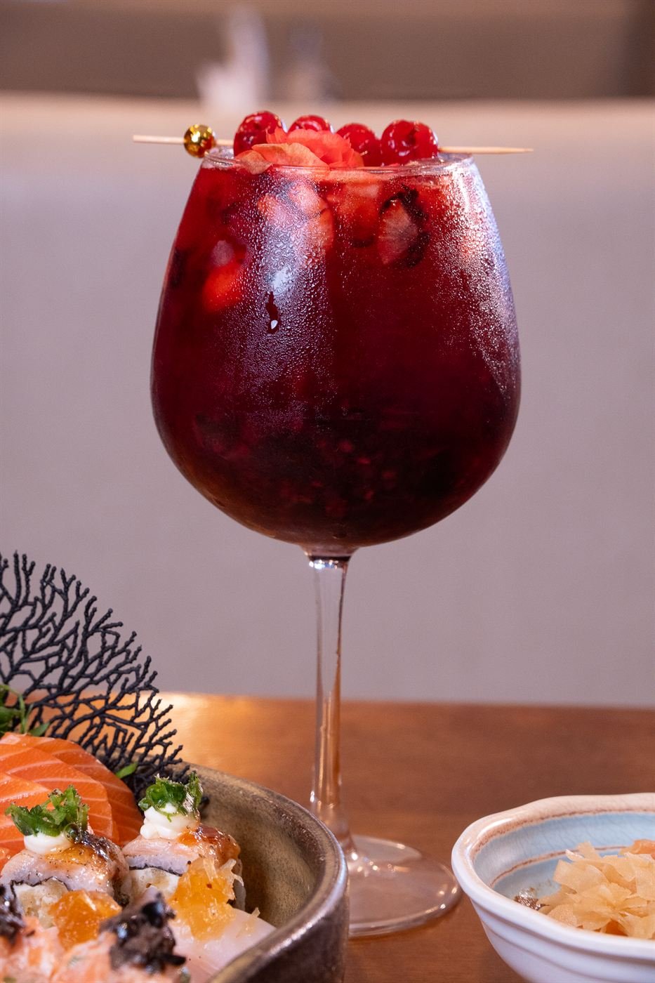 Drink vermelho com cerejas ao lado de sushi